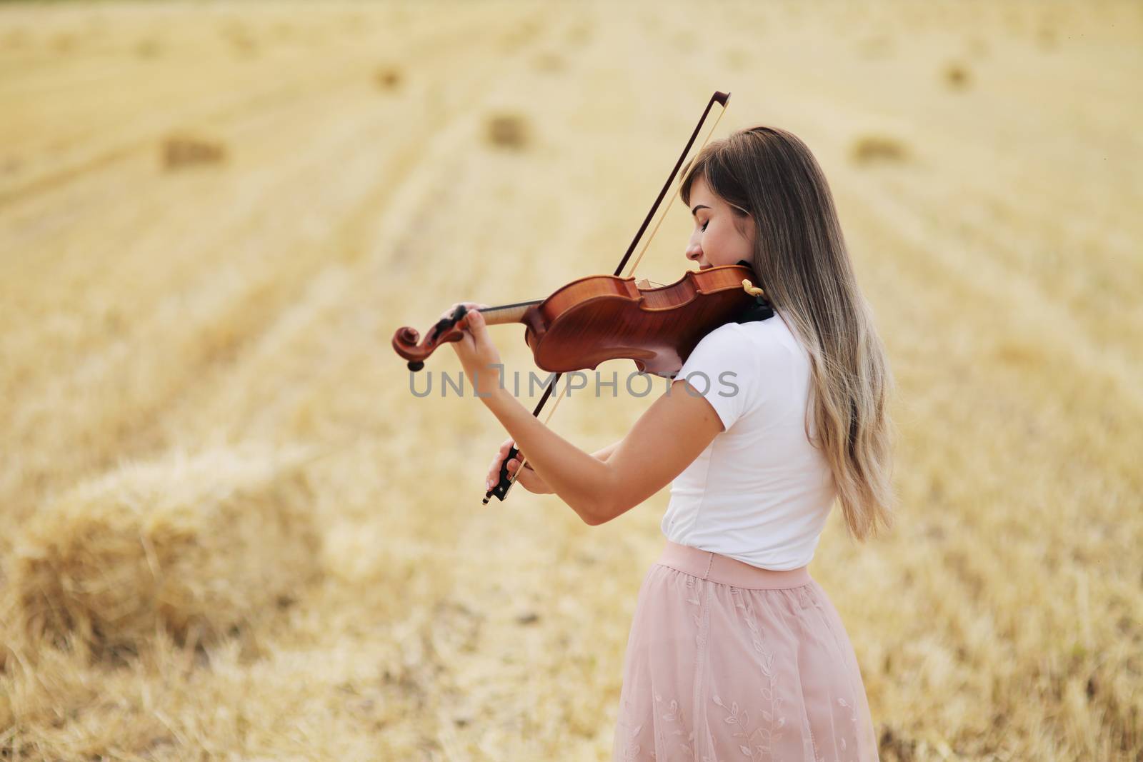 Beautiful romantic girl with loose hair playing the violin in the field. by selinsmo