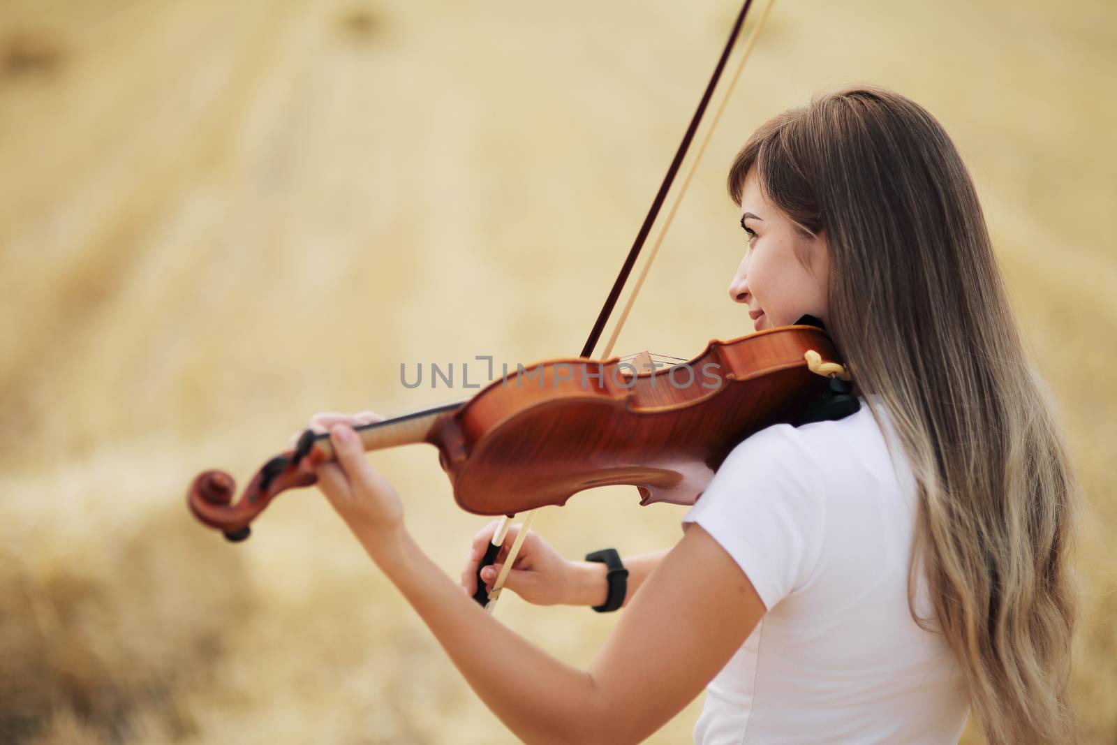 Beautiful romantic girl with loose hair playing the violin in the field. by selinsmo