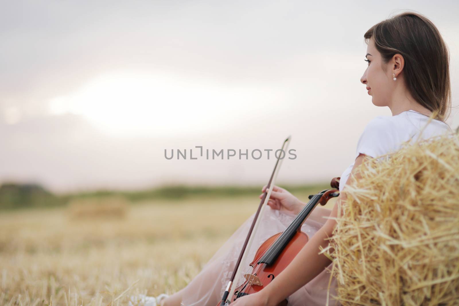 Romantic young woman with flowing hair holding a violin in her hand in a field by selinsmo