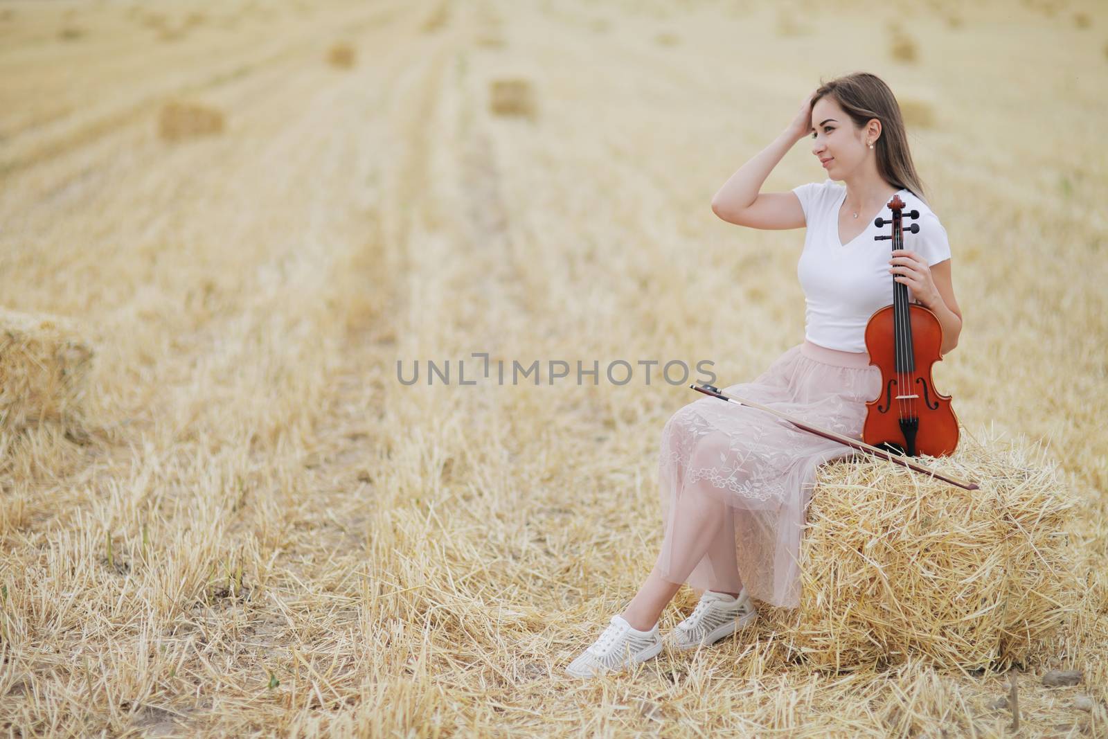 Romantic young woman with flowing hair holding a violin in her hand in a field by selinsmo