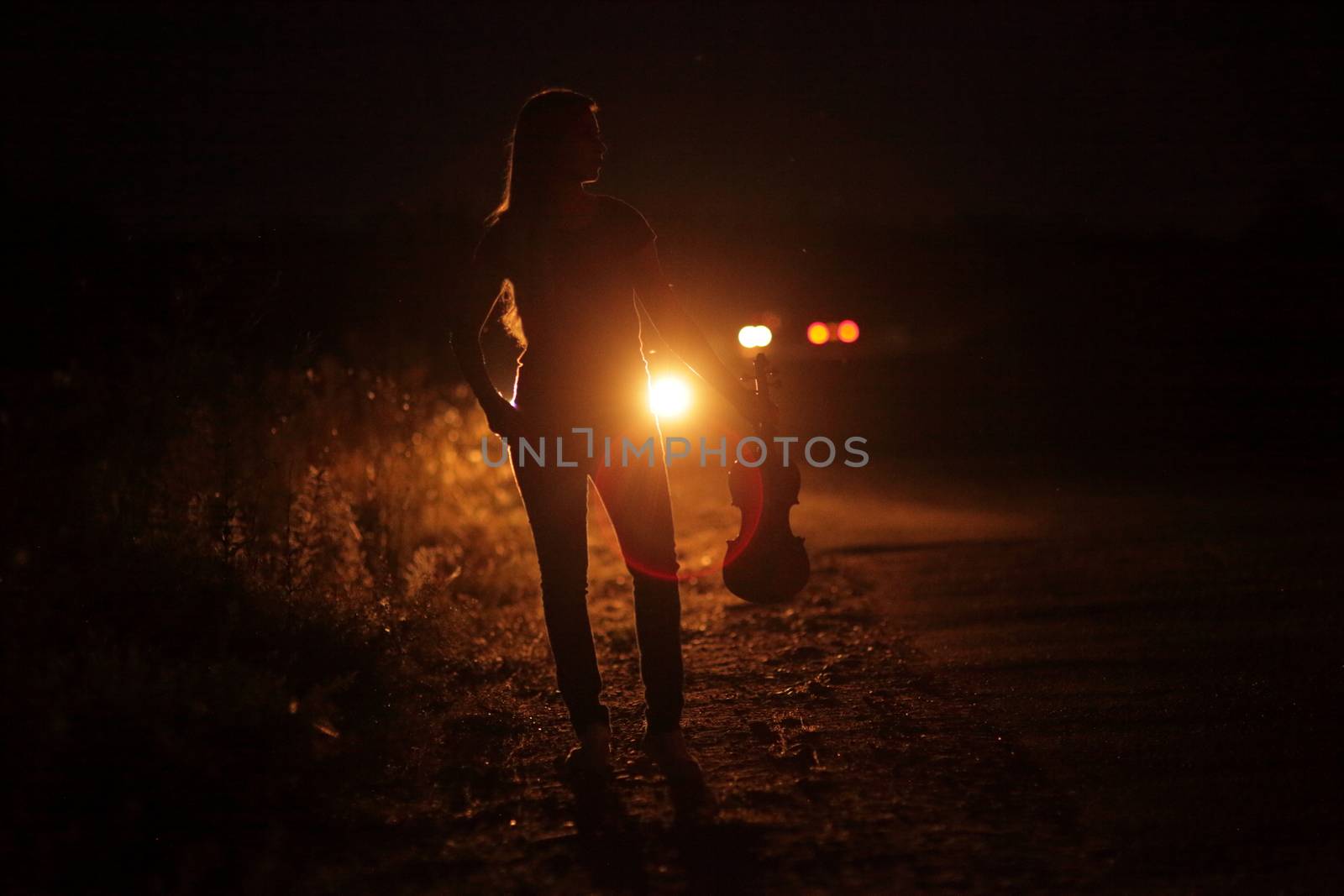 Silhouette of a slender young woman with violin in car headlights illumination by selinsmo