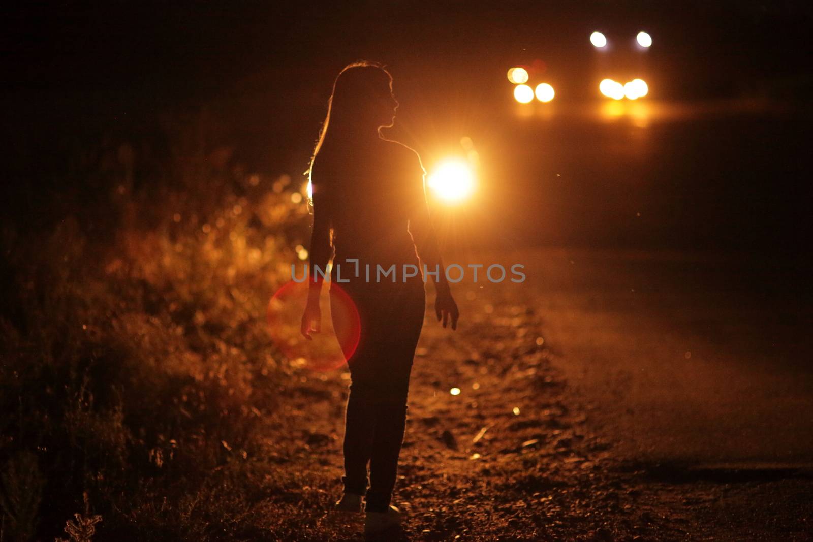 Silhouette of young slender woman in the backlight of car headlights on the road by selinsmo