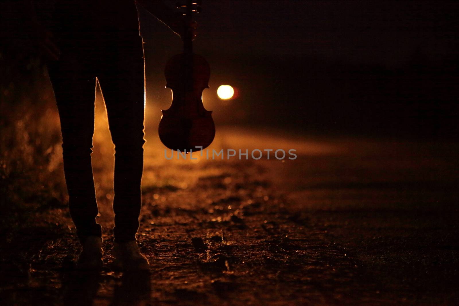 Silhouette of a slender girl's legs and a violin in the backlight of headlights by selinsmo