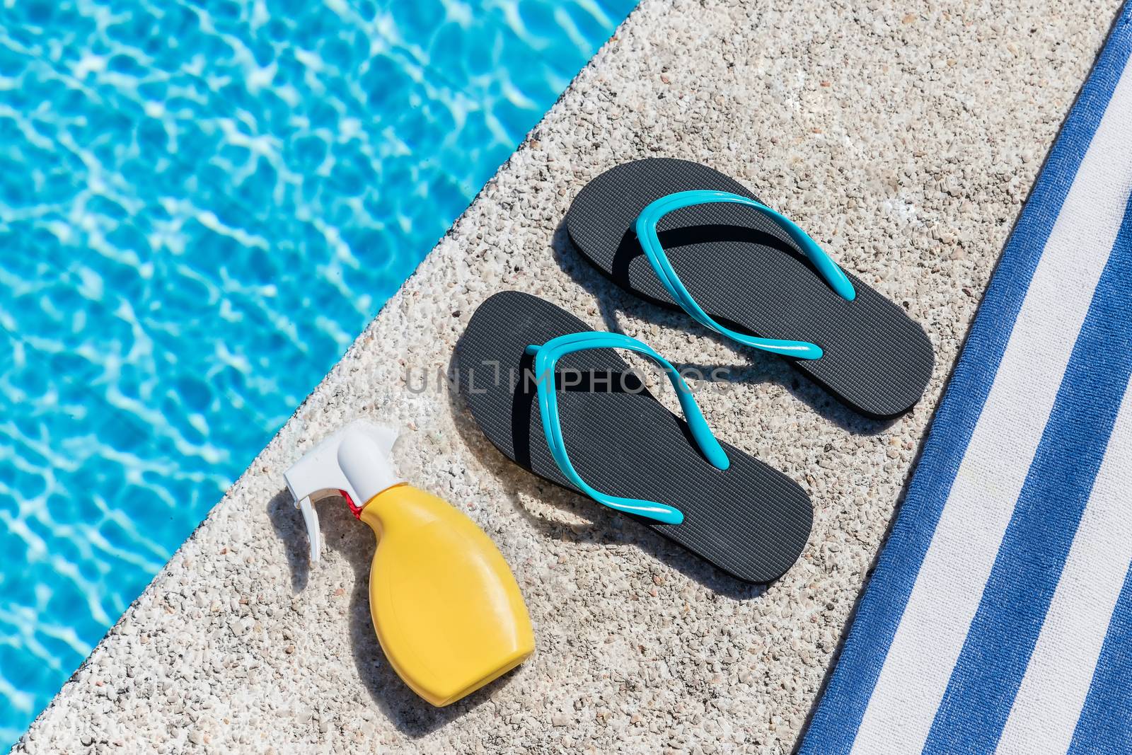 Flip flops, solar spray and a towel on the edge of a pool. Copy space. Top view.