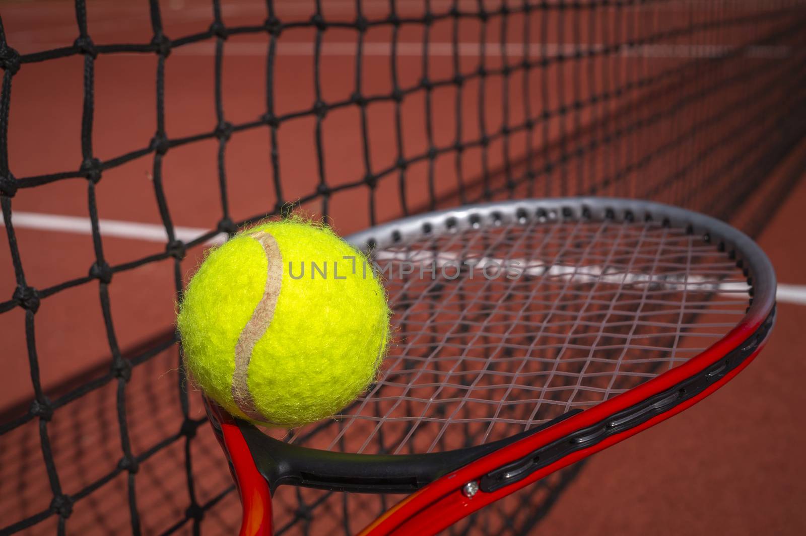 Tennis balancing ball on a racket alongside a net on a court in a sport and active healthy lifestyle concept