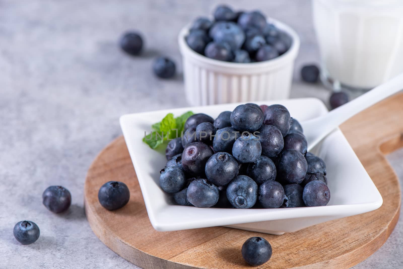 Pile of blueberry fruit in a bowl plate on a tray over gray cement concrete background, close up, healthy eating design concept.