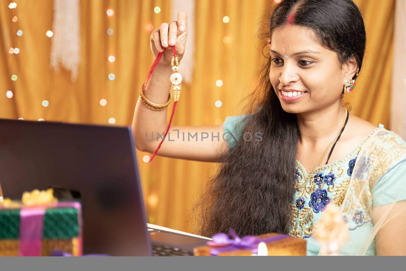 Indian Woman in tradition dress on video call or chat at Raksha Bandhan festival telling her brother to tie rakhi - Concept of distance relations, festival celebrations and technological lifestyle.