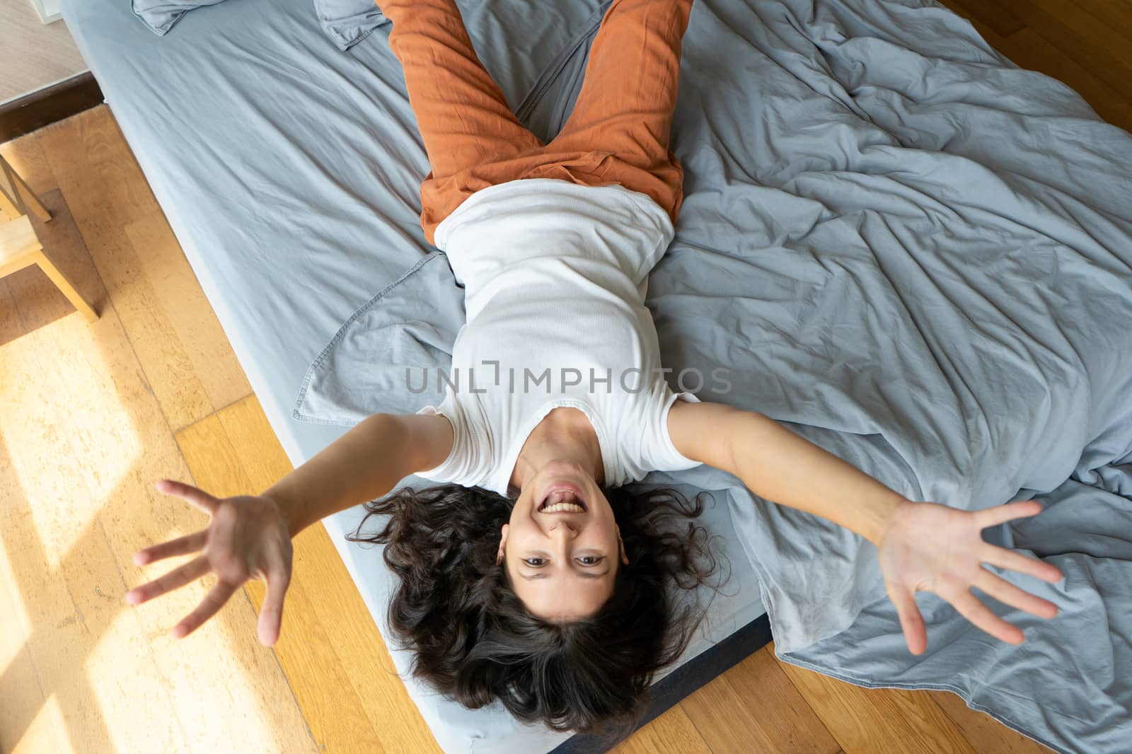 Beautiful young brunette girl fooling around on the bed. View from above. Good mood.