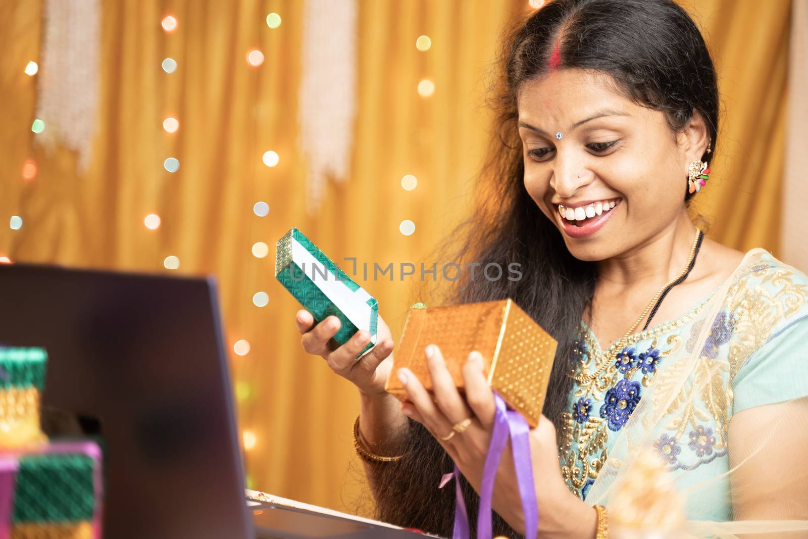 Happy excited Woman opening gift infront of laptop during video call or chat at Raksha Bandhan festival ceremony - Concept of distance relations, celebrations and lifestyle. by lakshmiprasad.maski@gmai.com