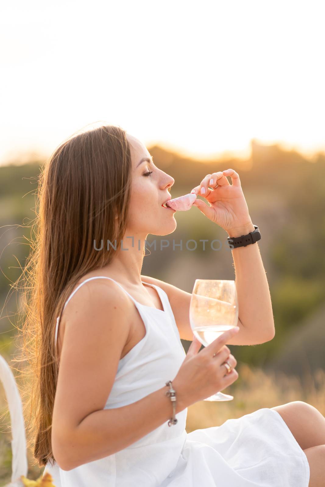 Gorgeous young brunette girl in a white sundress enjoying a picnic in a picturesque place. Romantic picnic.