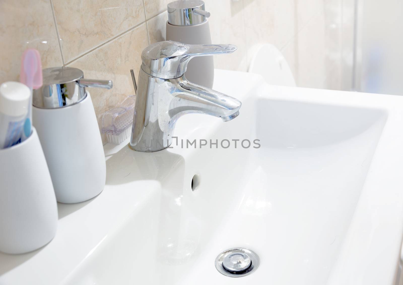 a white ceramic sink with a chromed tap with soap and toothbrush containers in a bathroom. Interior of a house.