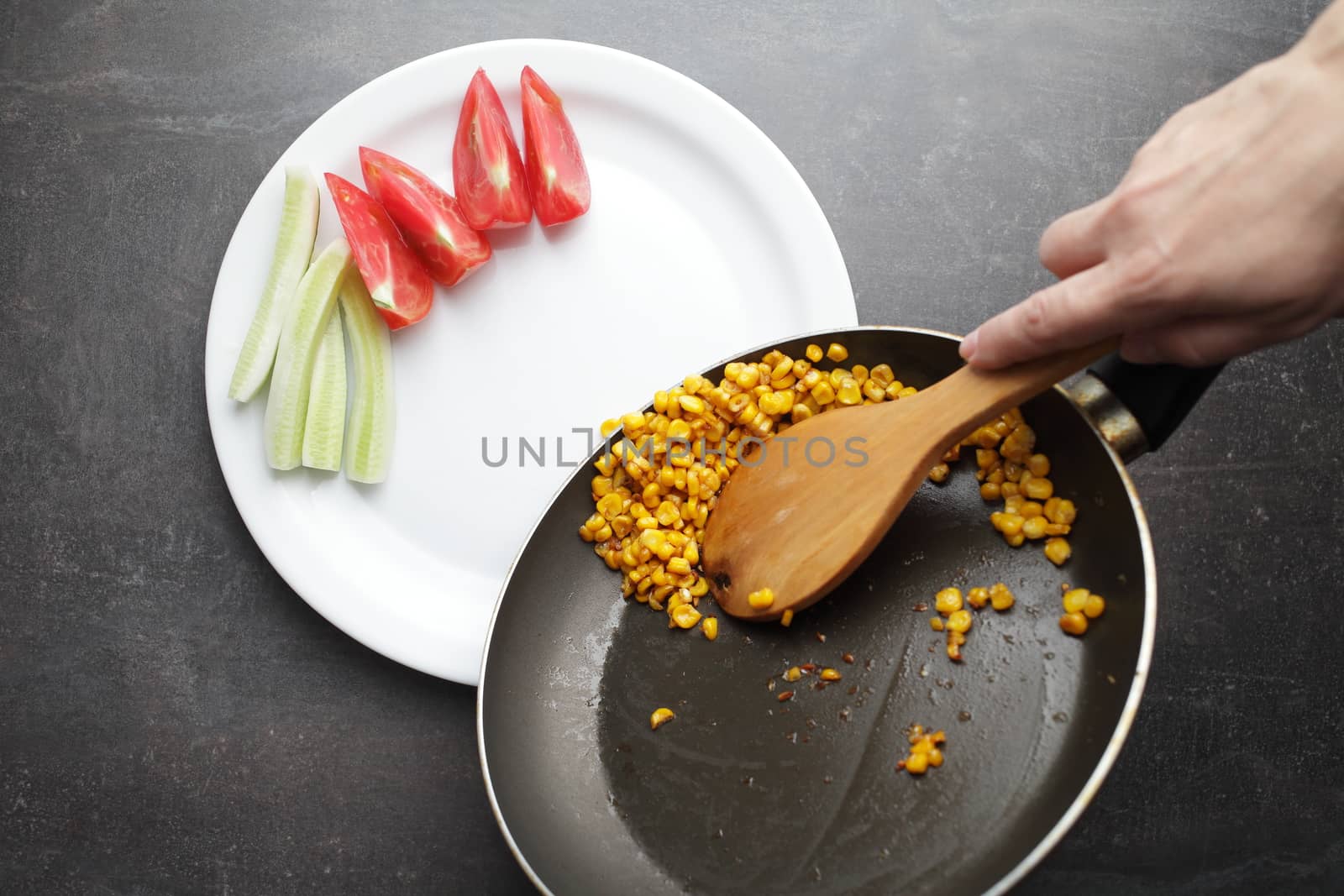 Diet. Organic Grilled Corn in a frying pan. Organic farm vegetables. Chopped tomato and cucumber on a white plate. Wooden spoon in hand. Environmentally friendly products