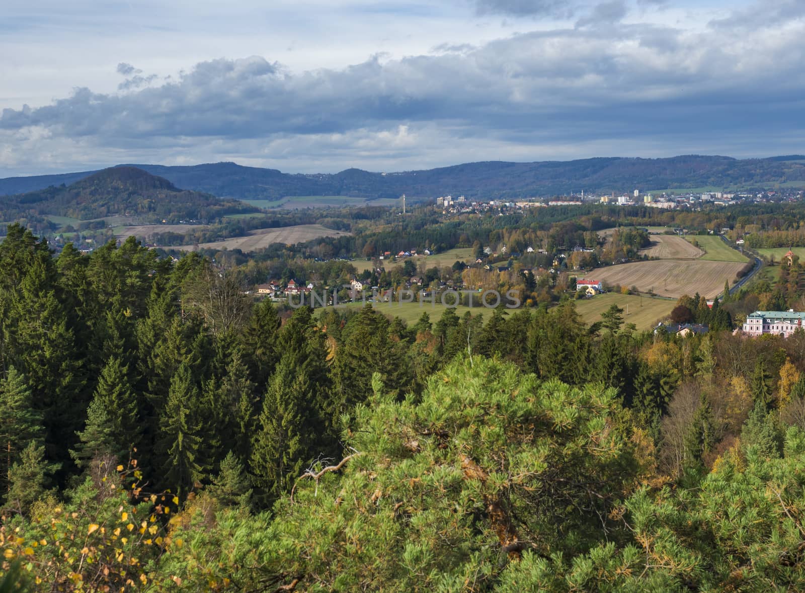 View from Hrabencina vyhlidka lookout on Novy bor town in luzicke hory, Lusatian Mountains with autumn colored deciduous and coniferous tree forest and green hills, blue sky, white clouds.