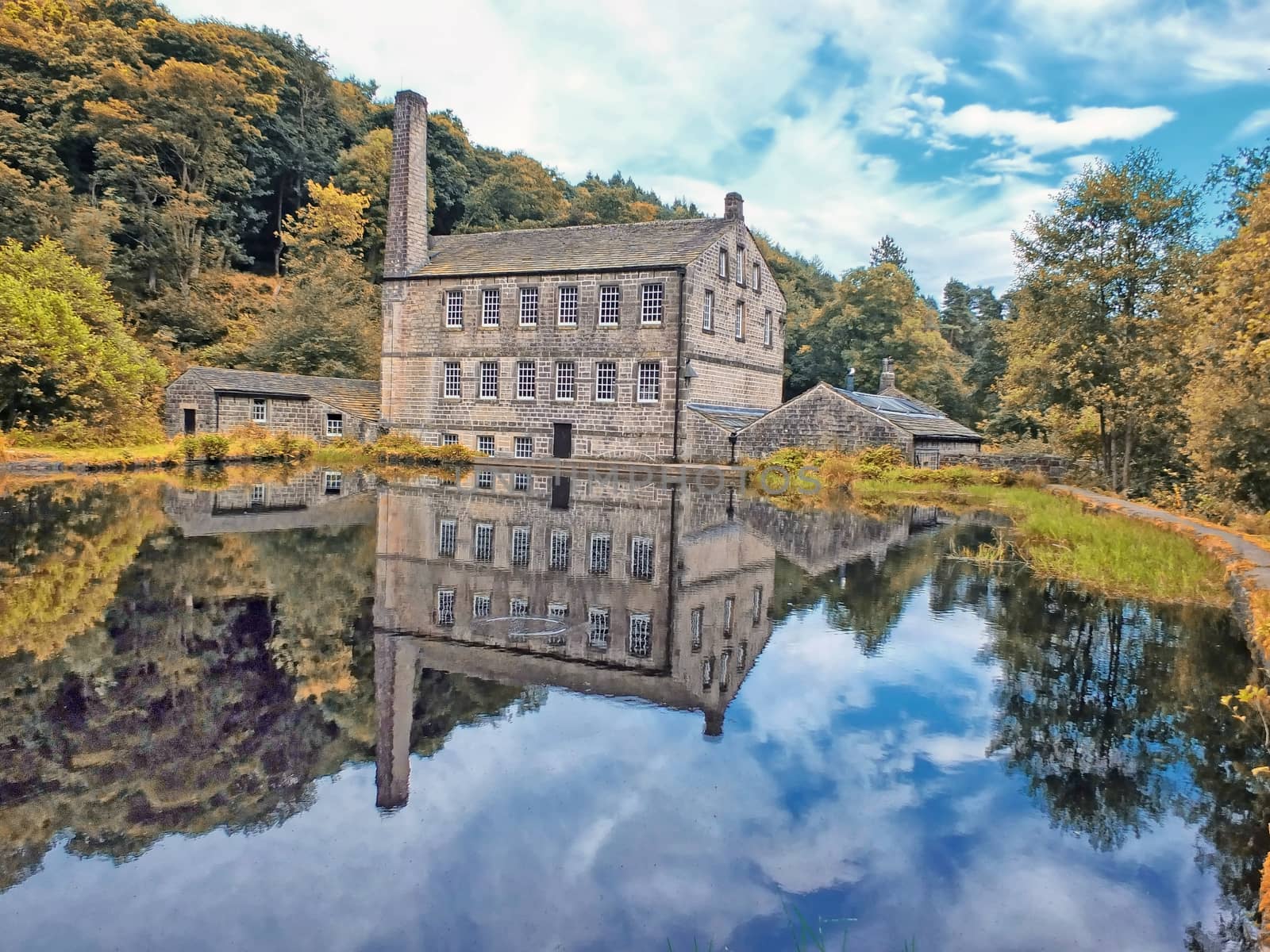 gibson mill a water powered mill with main bulding relected in the pond and surroounding trees of hardcastle crags near hebden bridge in west yorkshire