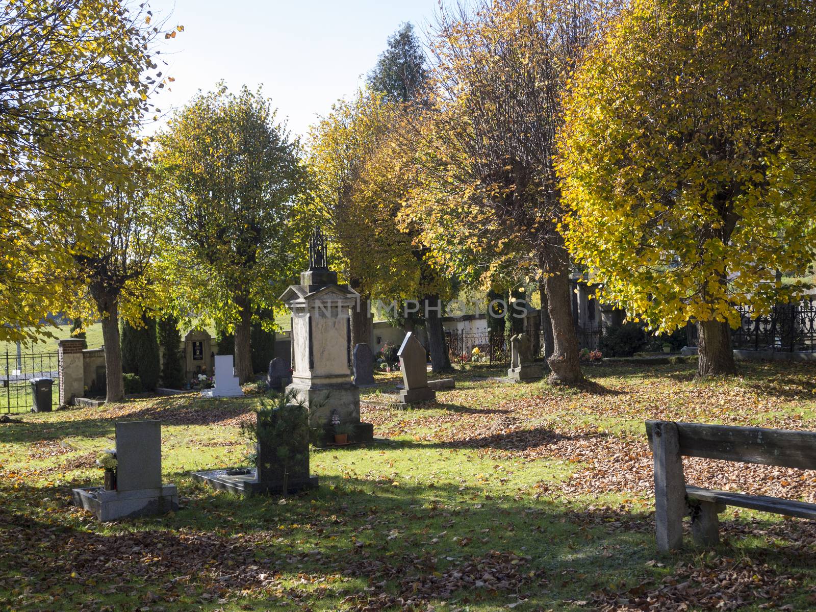 village cementery in autumn sunny day with bench graves and vault and golden lime trees