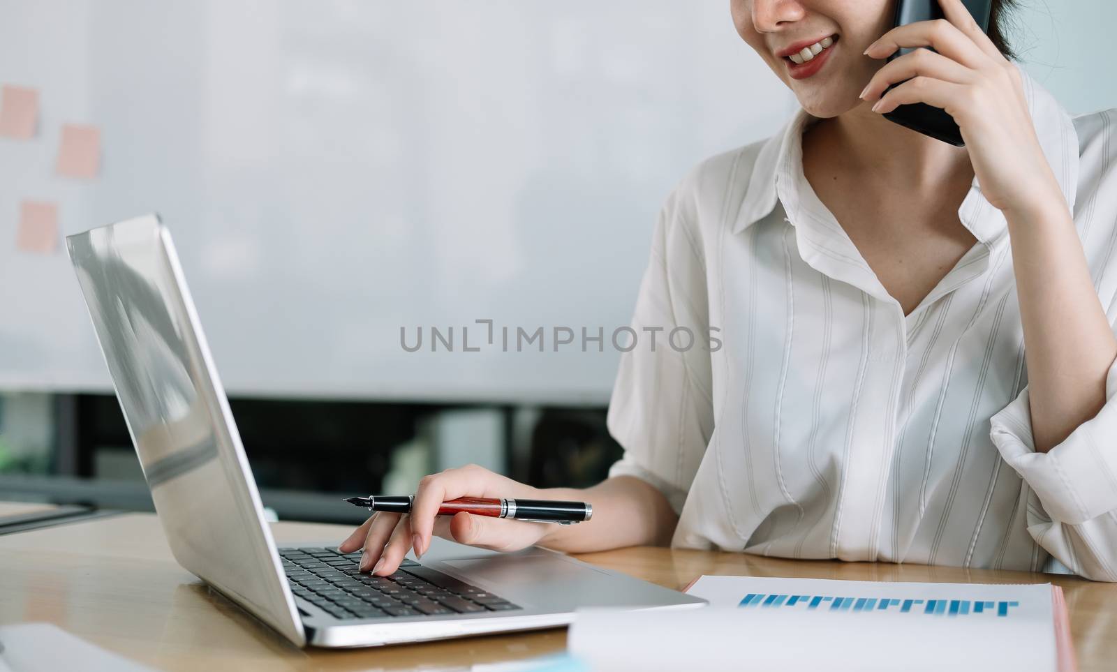 Young accountant hand holding smartphone to call marketing consultants and using laptop computer to analyze sales growth in the global workplace market. accounting concept.