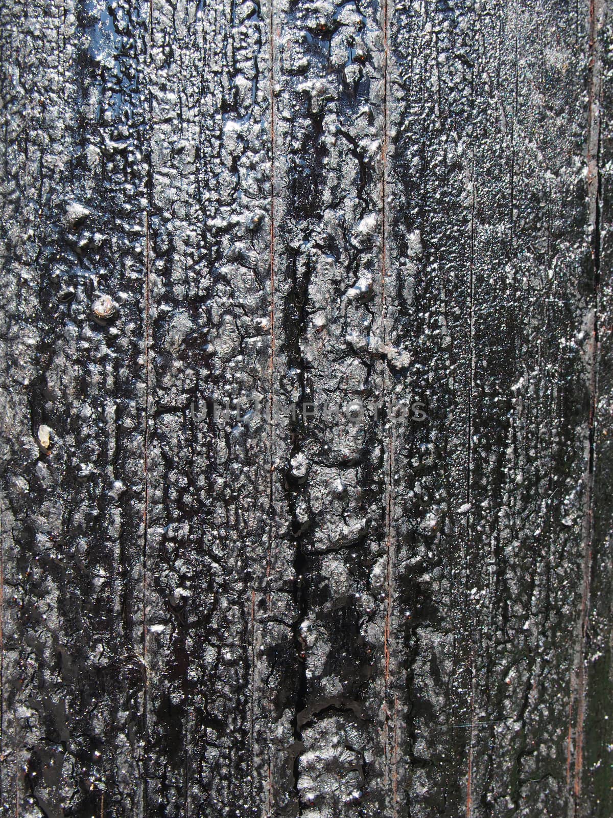 a black melting old bitumen preservative covered textured wooden surface by philopenshaw