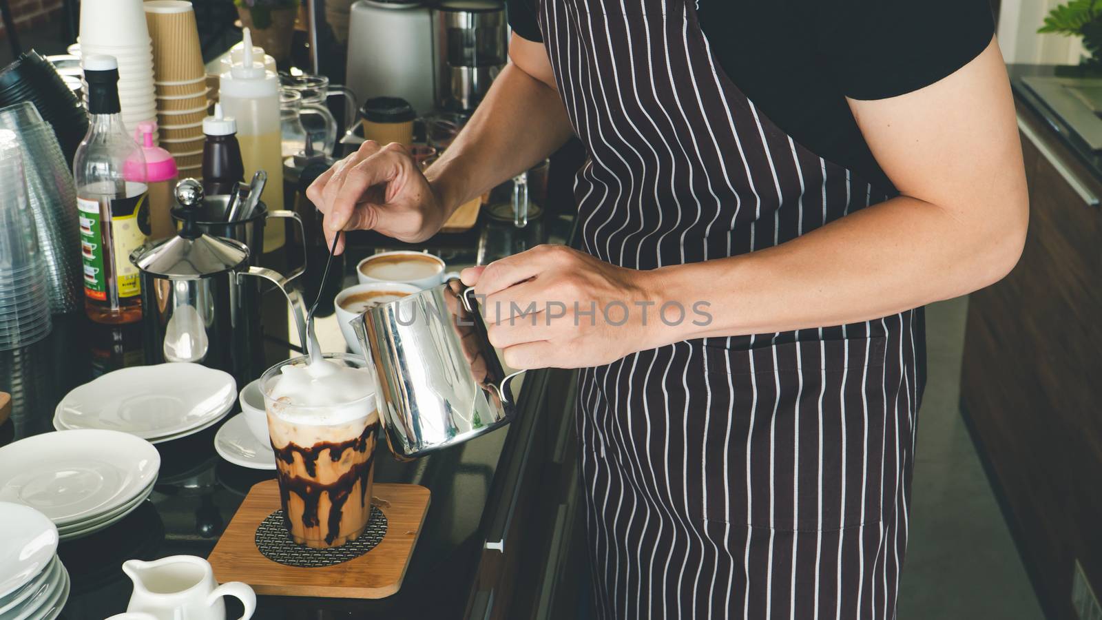 close-up photo of the hand is pouring freshly made cappuccino into a glass. barista Professional men making latte and espresso for customer service.  coffee shop owner is preparing drinks in the cafe.