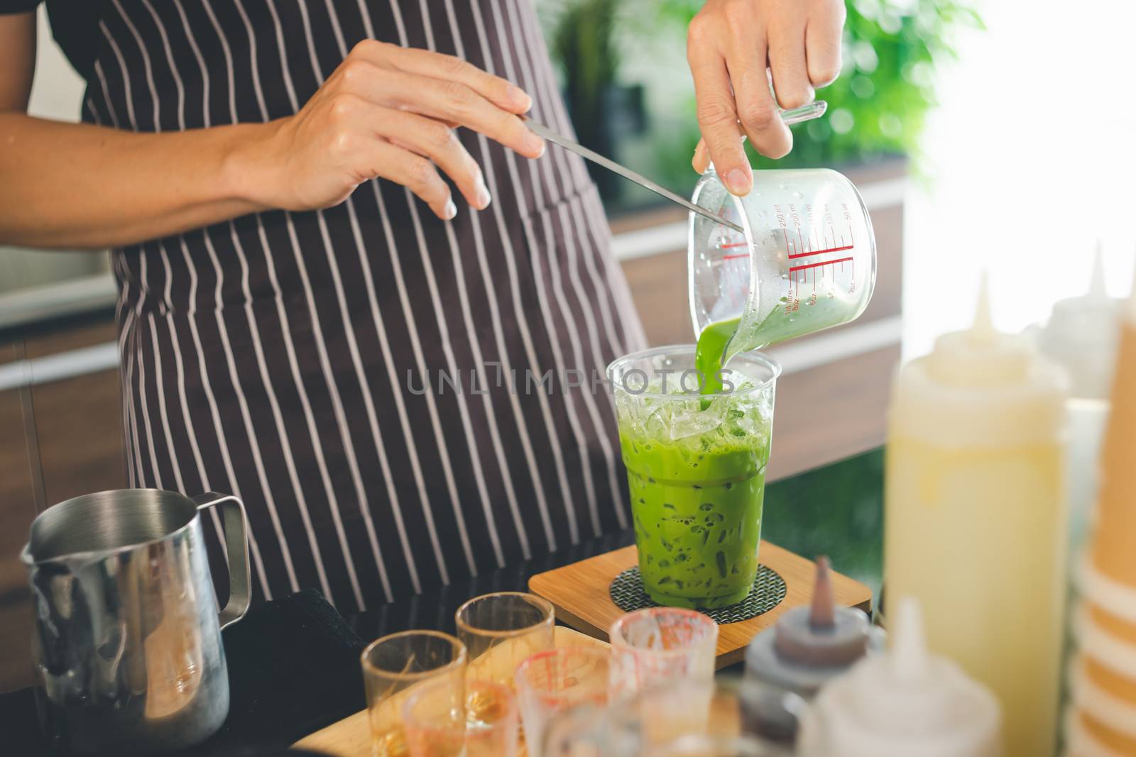 A close-up shot of a man pouring a freshly made green tea into a glass. barista is making matcha tea for customer service. Coffee shop business owners are preparing drinks in the cafe