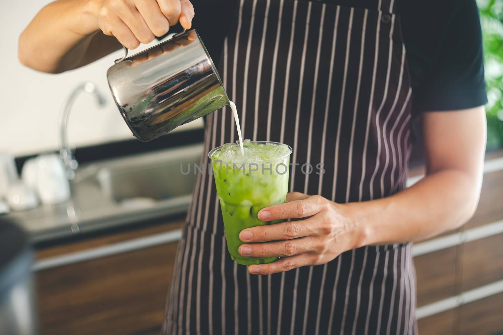 close-up of a man's hand pouring milk into a freshly made green tea glass. barista is making matcha tea for customer service. Coffee shop business owners are preparing drinks in the cafe