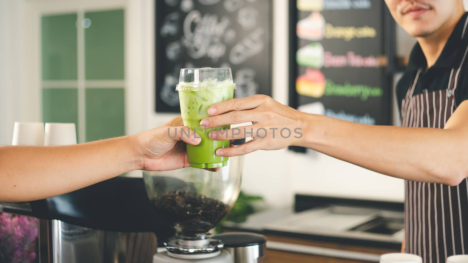 close-up of a man's hand is holding a glass of freshly made green tea for the customer. barista is making matcha tea for service. Coffee shop business owner is preparing drinks in the cafe