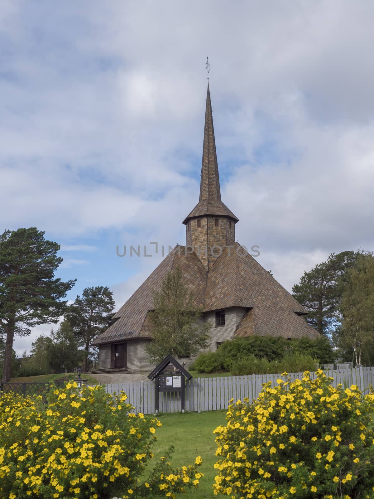 The old church of Dombas in traditional style with blooming yellow flowers. Blue sky, white cloud background. Oppland, Norway.