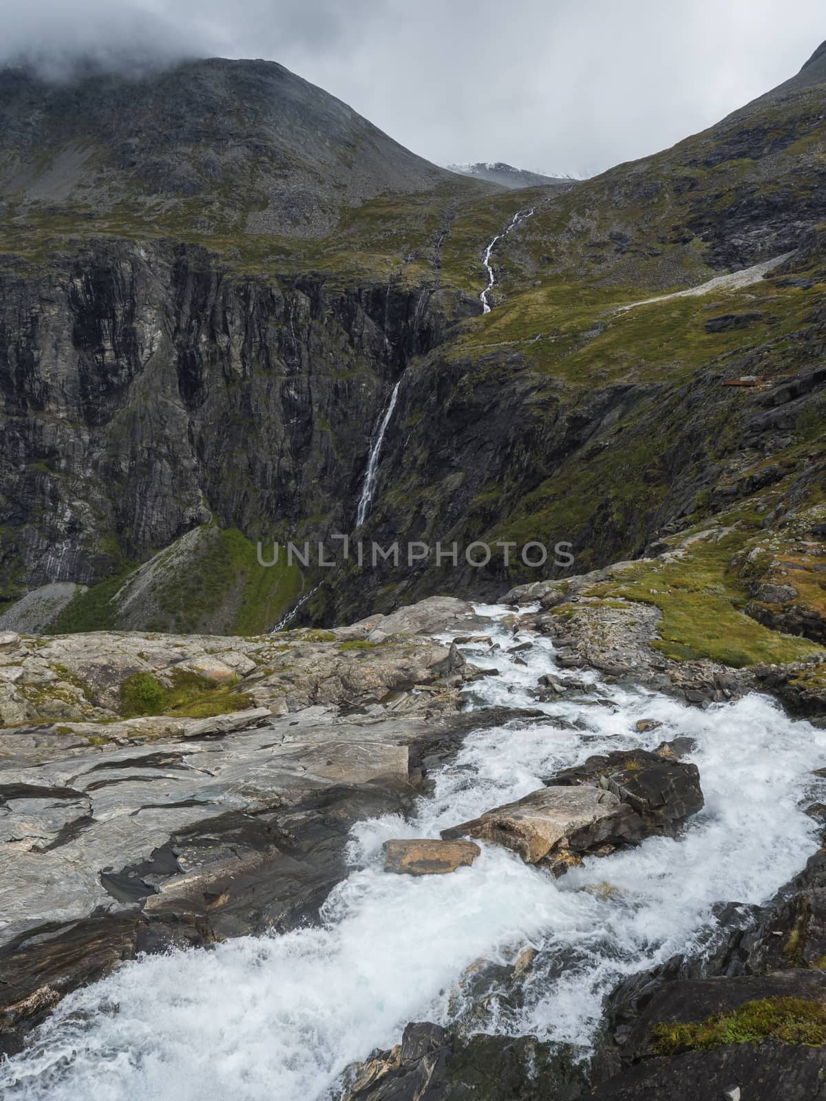 View point platform on Trollstigen or Trolls Path with green valley and waterfall at massif Trolltindene in Romsdal valley, Norway. Cloudy white sky clouds. by Henkeova