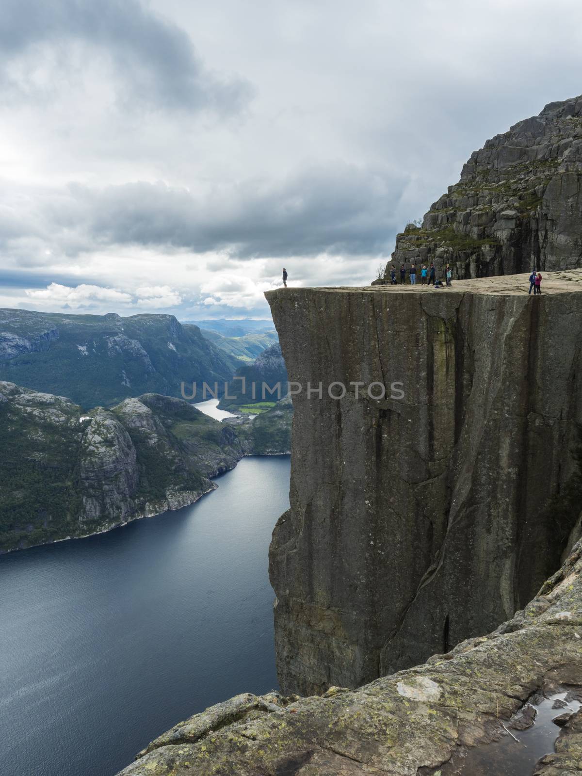 Profile view of famous Preikestolen massive cliff at fjord Lysefjord, famous Norway viewpoint with group of tourists and hikers. Moody autumn day. Nature and travel background, vacation and hiking holiday concept. by Henkeova