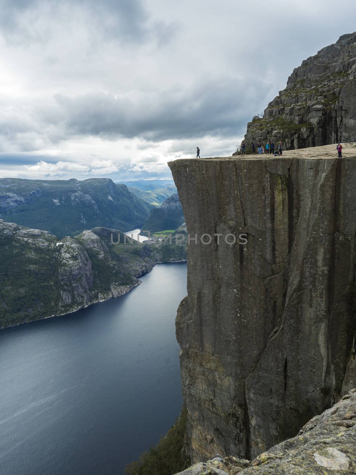 Profile view of famous Preikestolen massive cliff at fjord Lysefjord, famous Norway viewpoint with group of tourists and hikers. Moody autumn day. Nature and travel background, vacation and hiking holiday concept