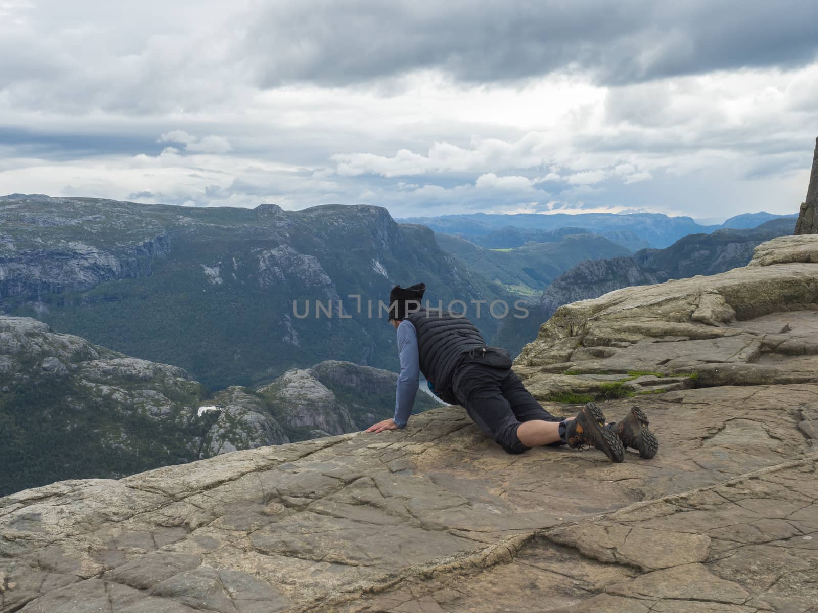 Lying men looking view on fjord Lysefjord over the Preikestolen cliff, famous Norway viewpoint. Moody autumn day. Nature and travel background, vacation and hiking holiday
