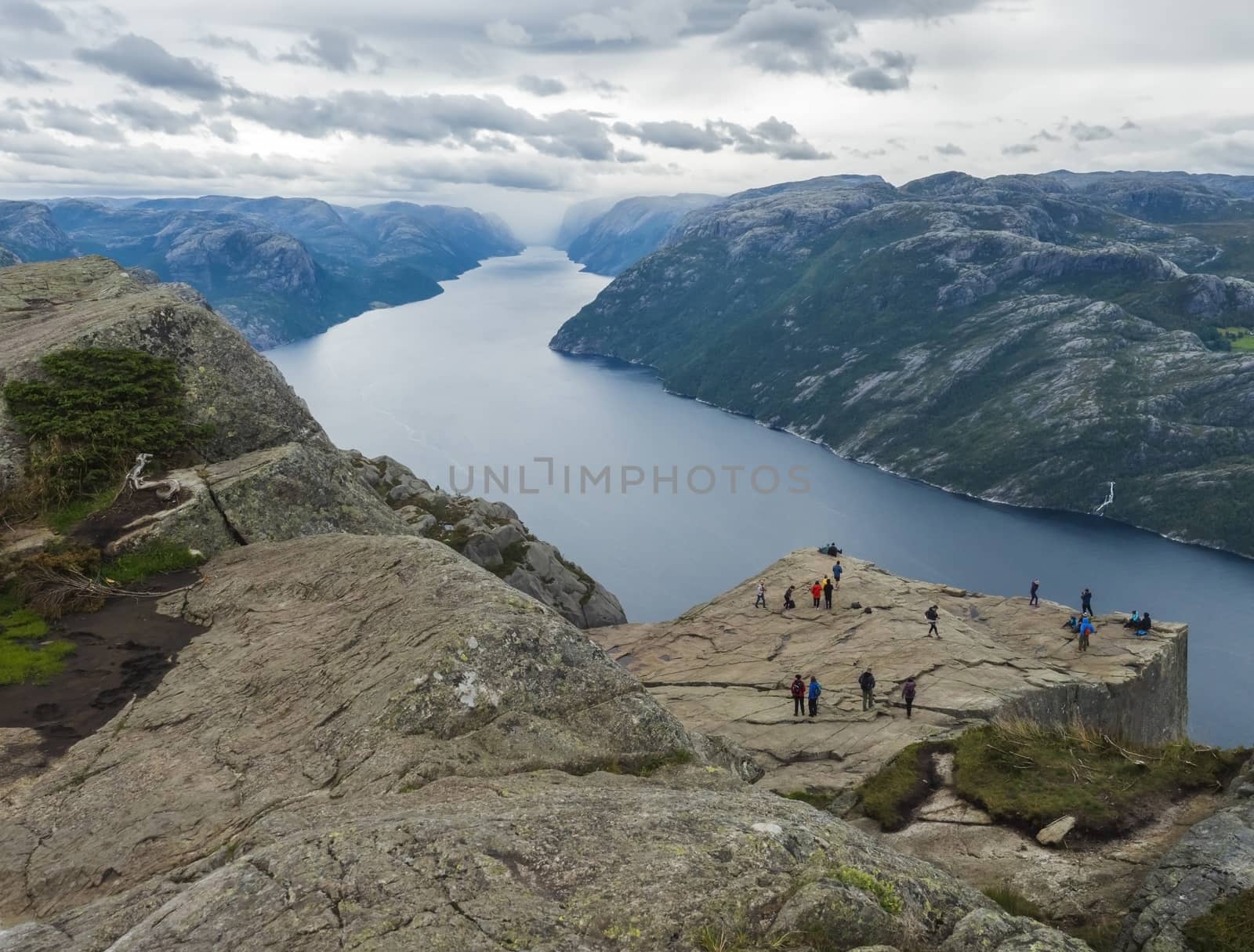 Preikestolen massive cliff at fjord Lysefjord, famous Norway viewpoint with group of tourists and hikers.Moody autumn day. Nature and travel background, vacation and hiking holiday concept. by Henkeova