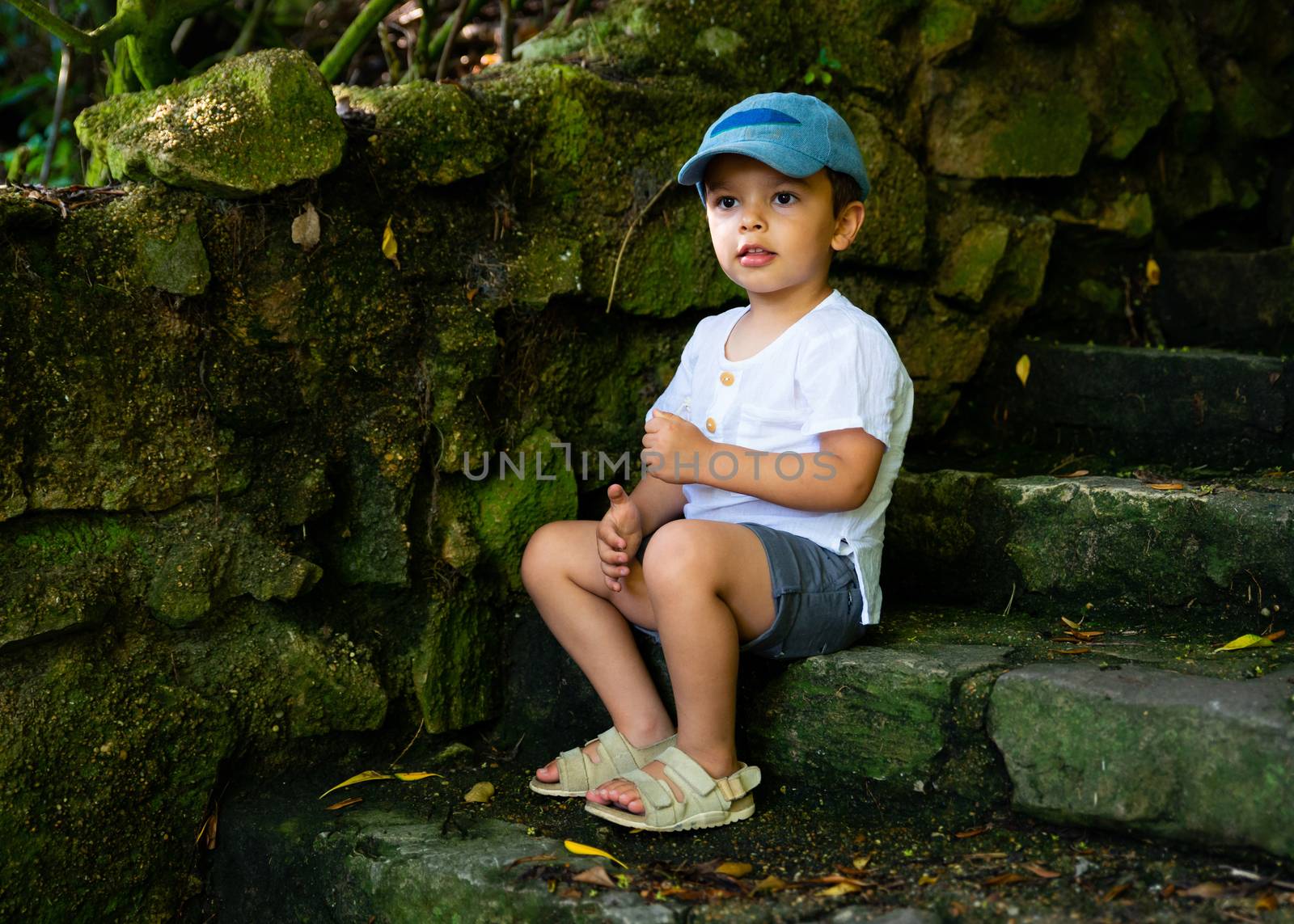 Little boy sitting on old stone stairs in the shade