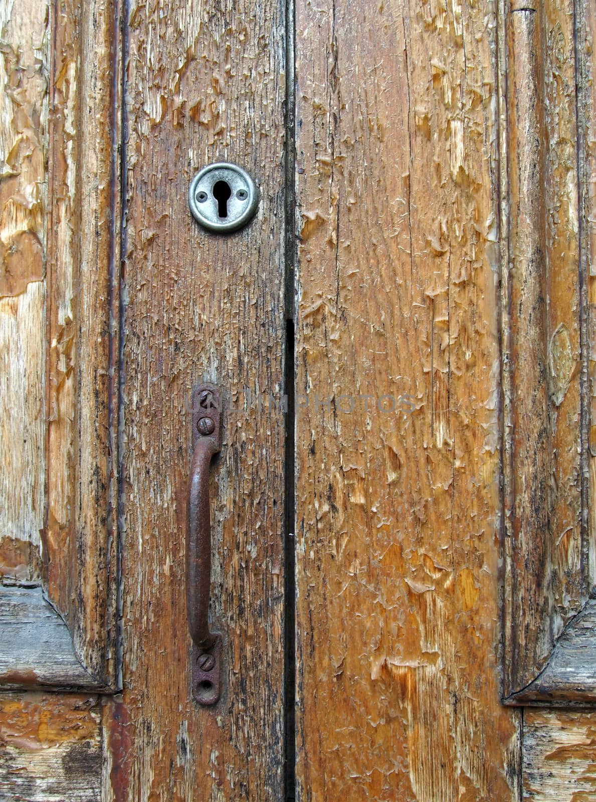 close up of an old brown varnished peeling wooden door with keyhole and rusty handle