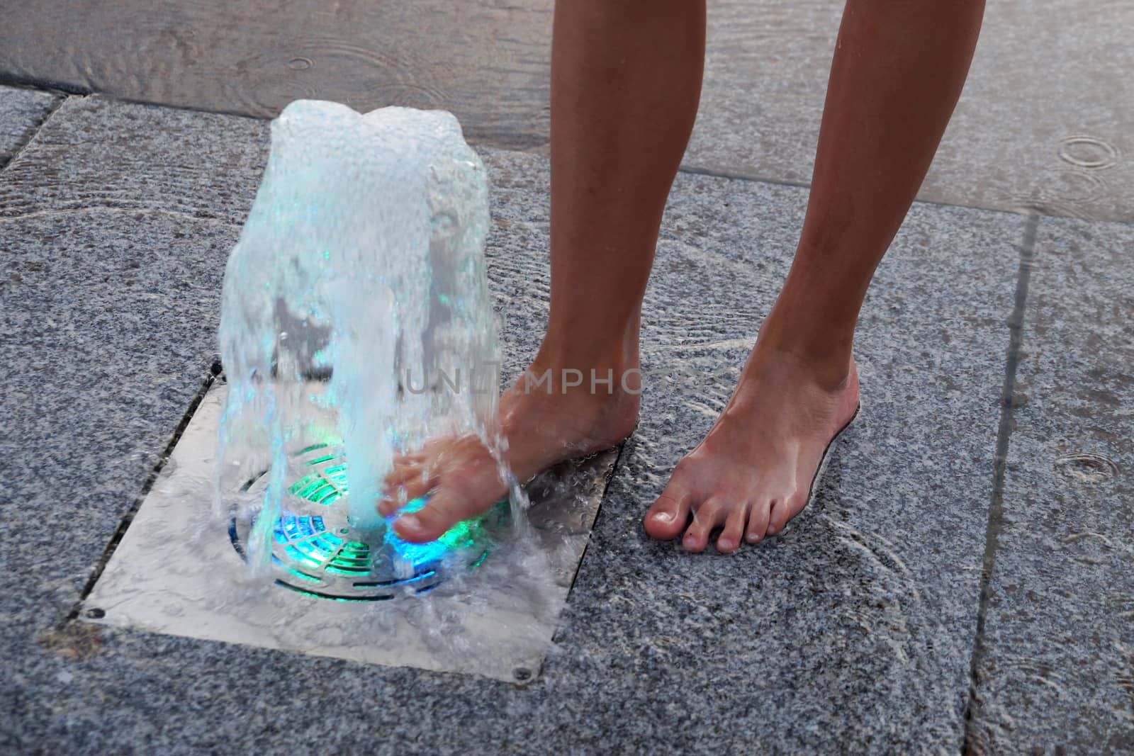 feet of a girl near a colored fountain on the sidewalk