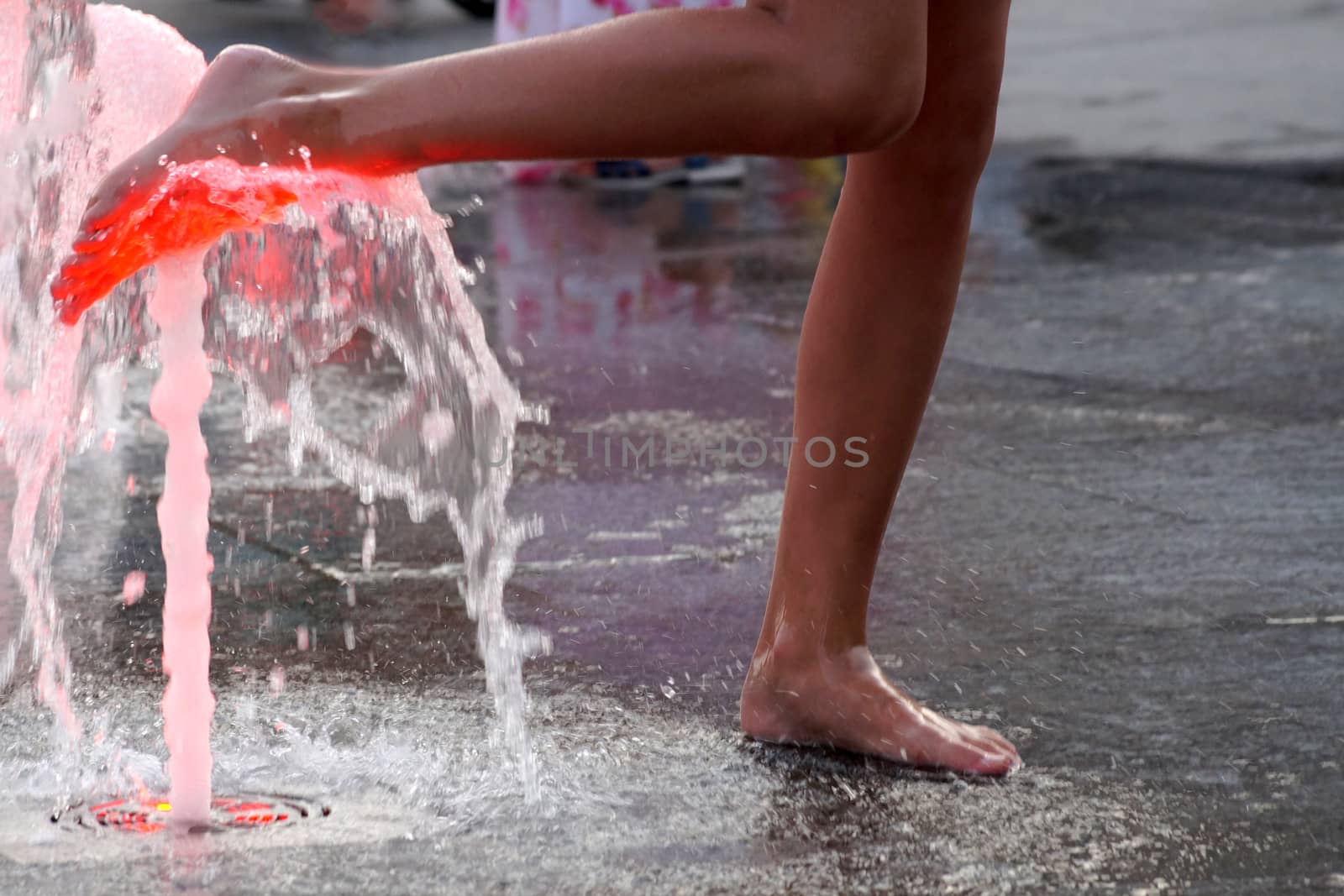 a girl touches a fountain on the sidewalk with her bare foot.