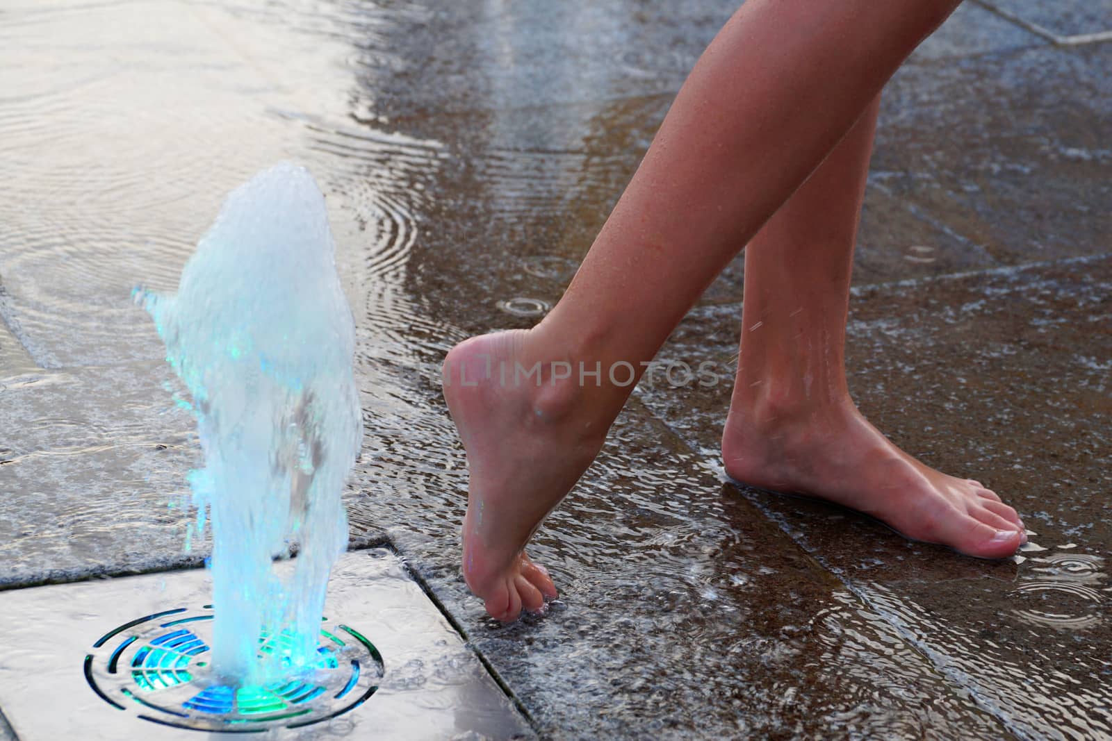feet of a girl near a colored fountain on the sidewalk