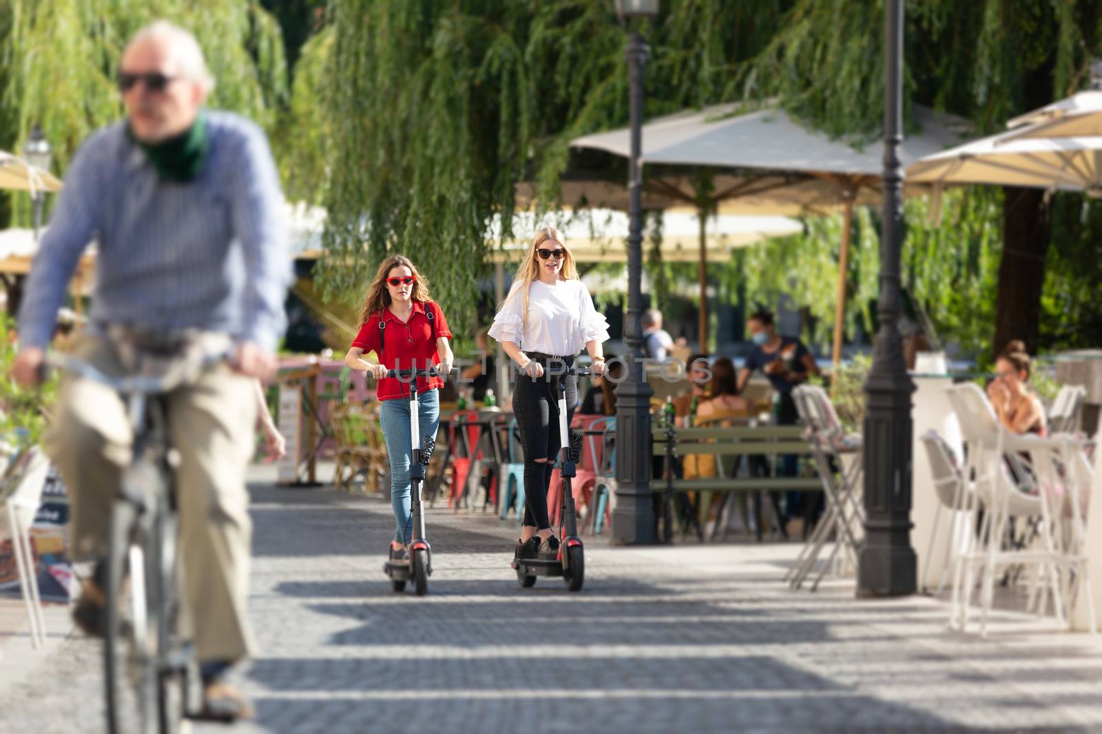 Trendy fashinable teenager girls riding public rental electric scooters in urban city environment. New eco-friendly modern public city transport in Ljubljana, Slovenia.