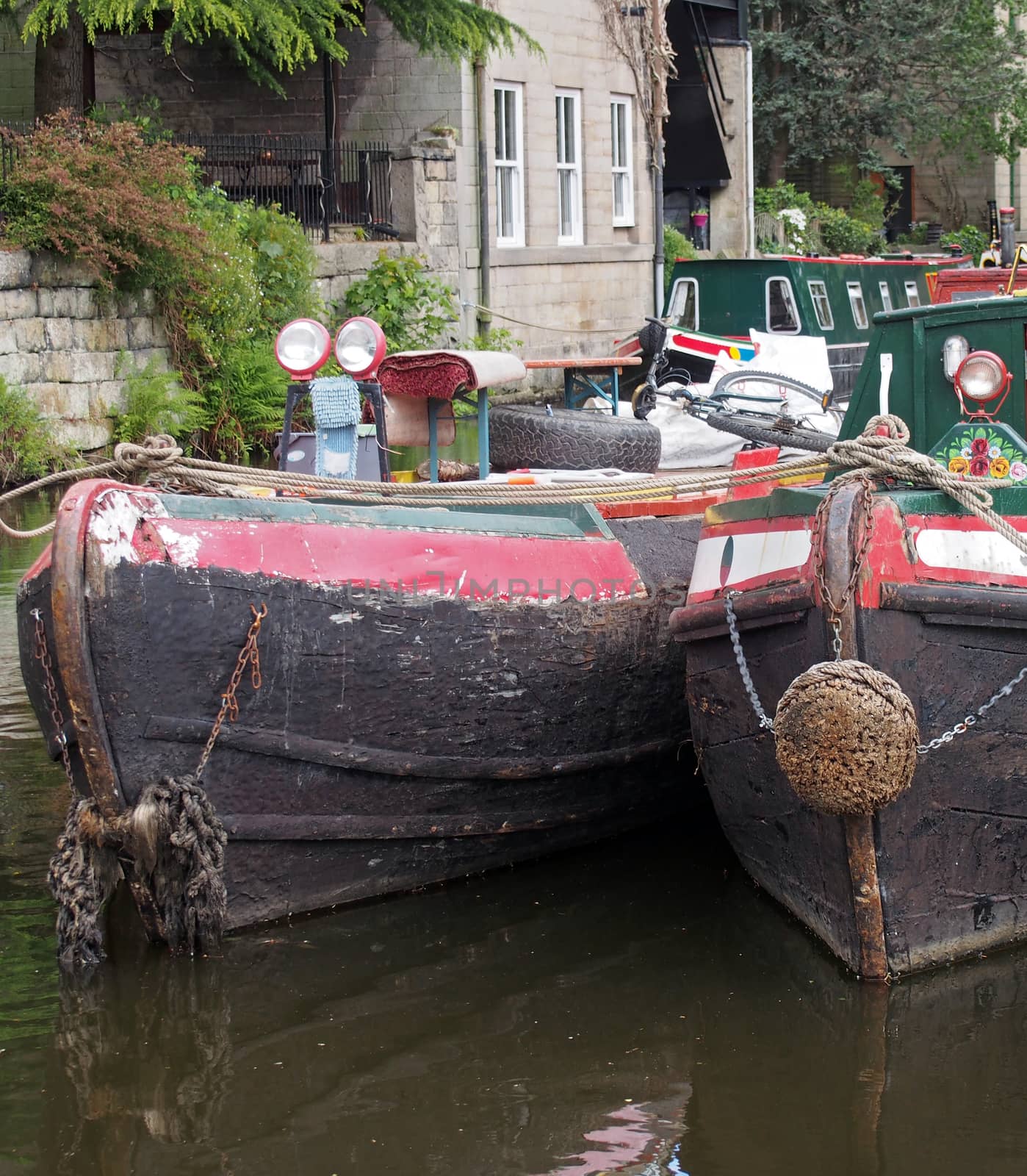 the bows of two old moored narrow boat on the rochdale canal in hebden bridge surrounded by grass trees and old buildings