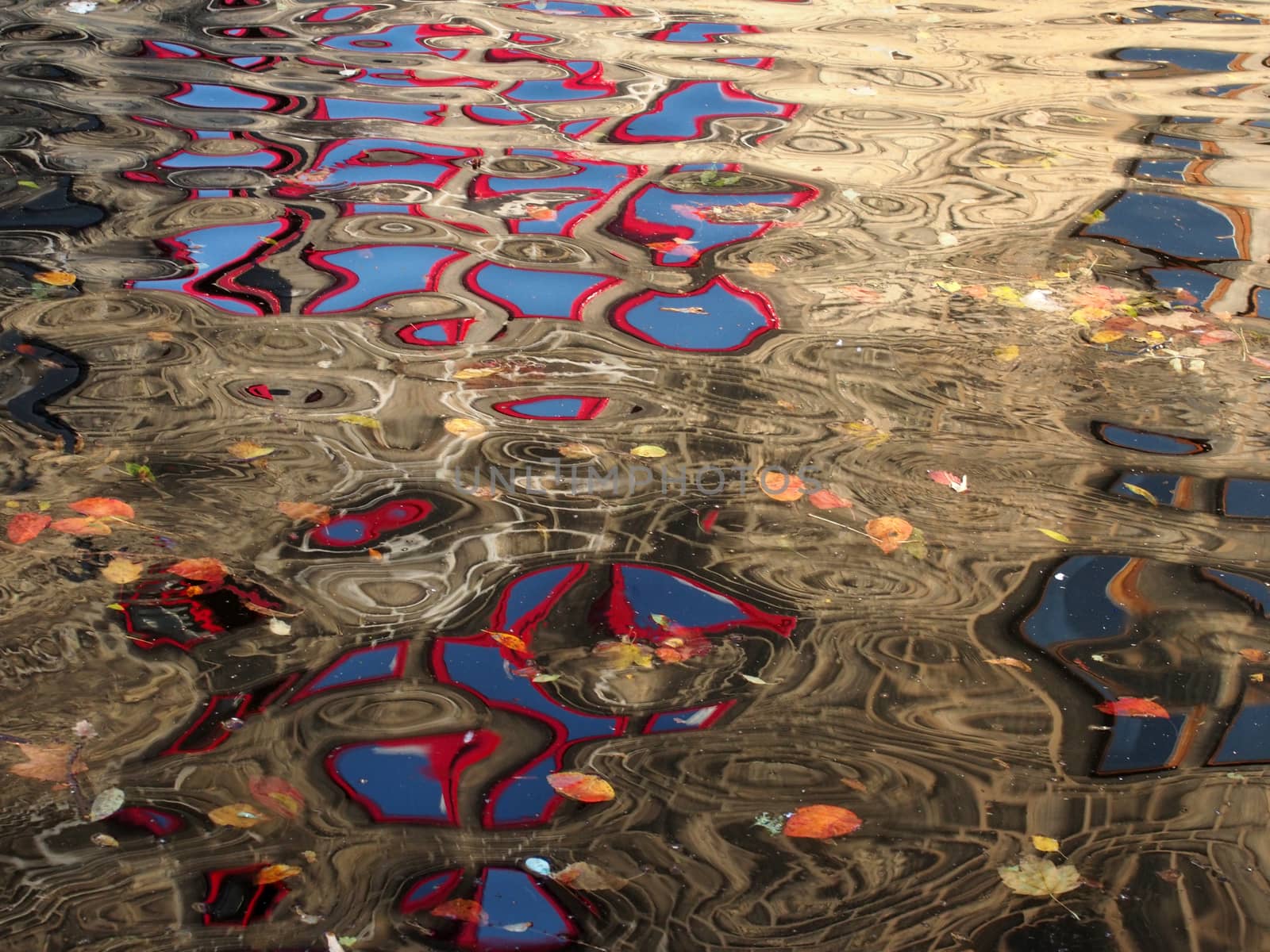 abstract image of red windows of an old stone building reflected in the ripples of dark water with floating autumn leaves