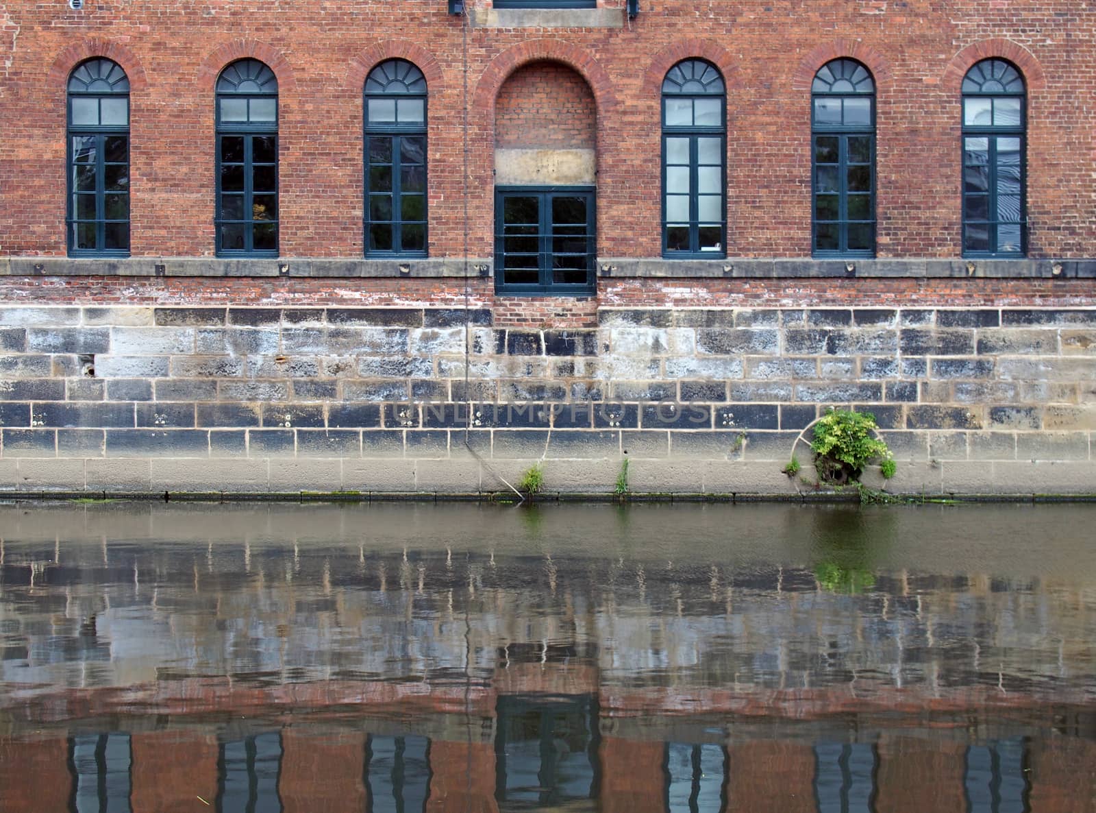 an old brick canal warehouse in leeds with windows reflected in the water