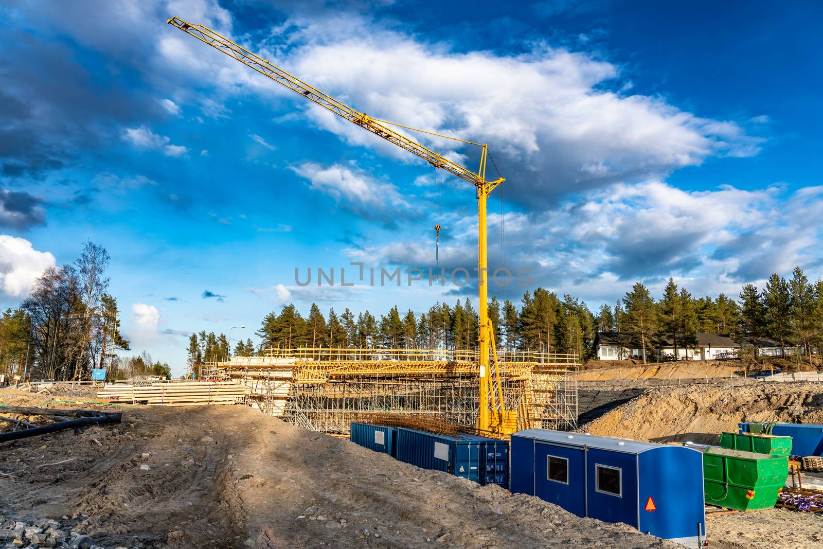 Photo of new bridge building site with timbering construction for further filling it with concrete. Yellow crane tower, blue clouds, deep ditch. A lot of building materials - steel and wooden parts by skydreamliner