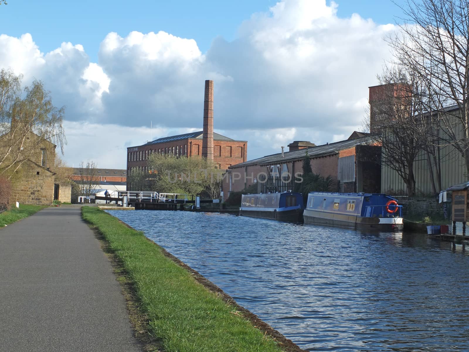the historic castleton mill near armley in leeds and oddy lock gates and footbridge crossing the canal with moored houseboats by philopenshaw