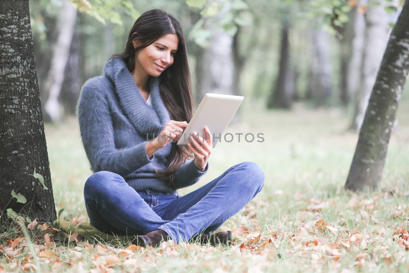 Smiling young woman using digital tablet sitting in autumn park