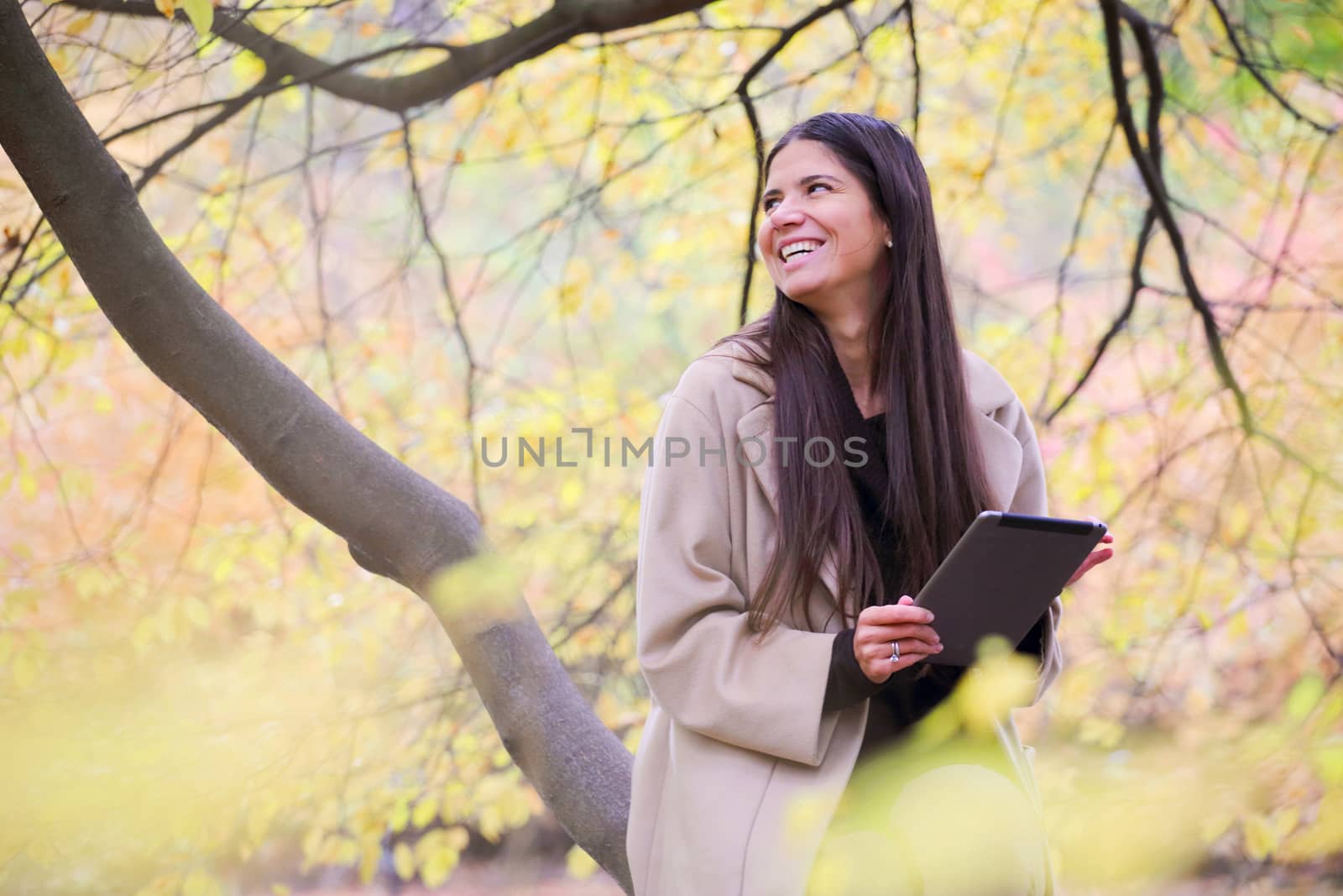 Smiling young woman using digital tablet sitting in autumn park