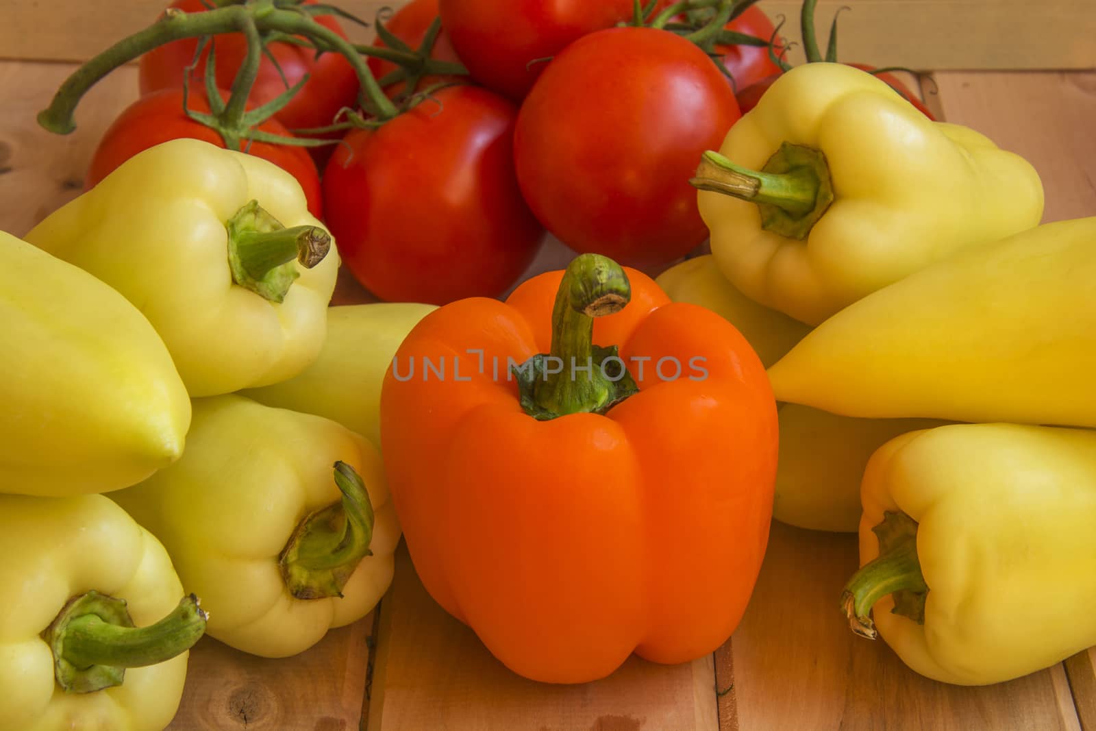 Orange and green peppers with tomatoes branch on a wooden surfac by Grommik