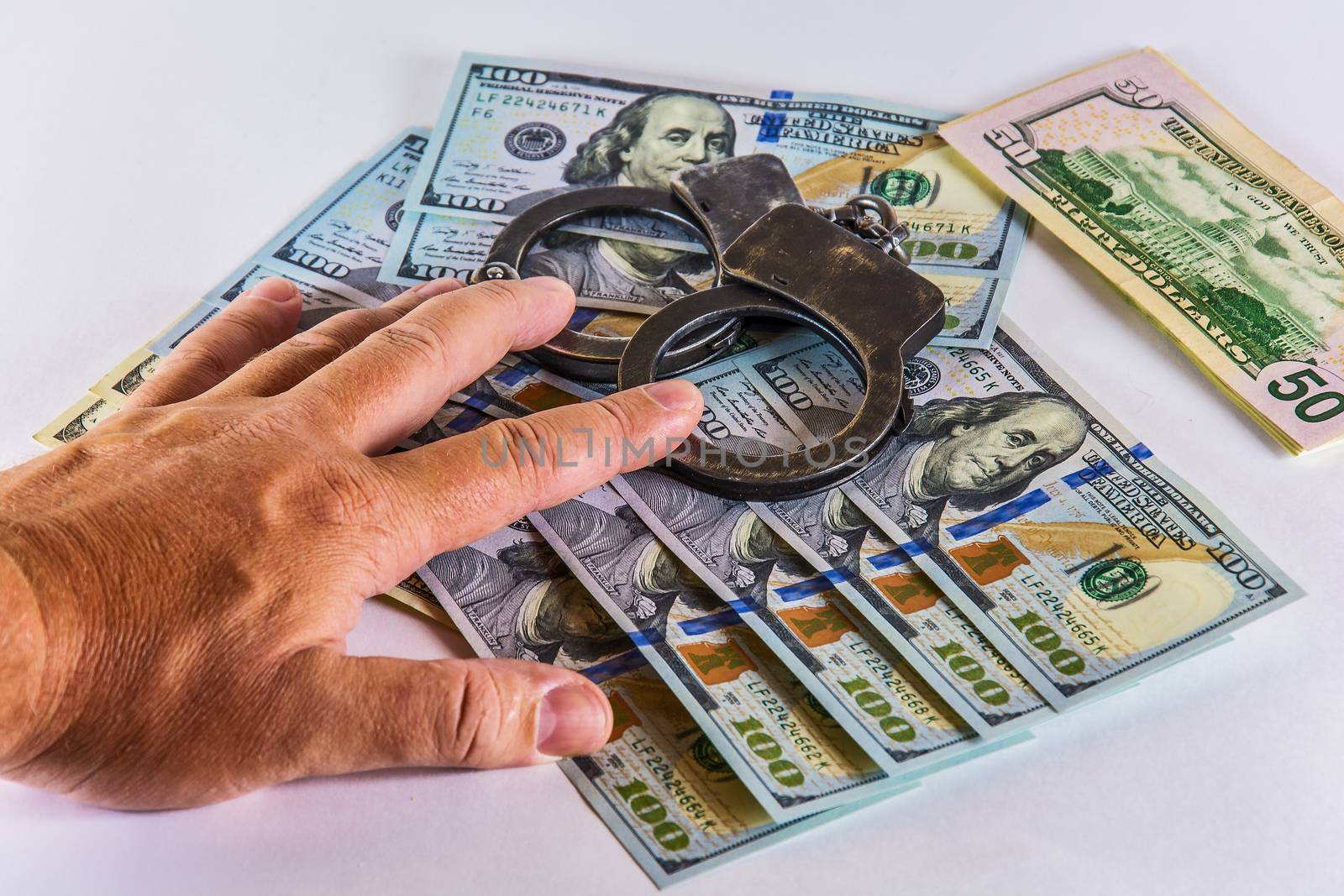 Man's hand covers the handcuffs and US dollars by Grommik