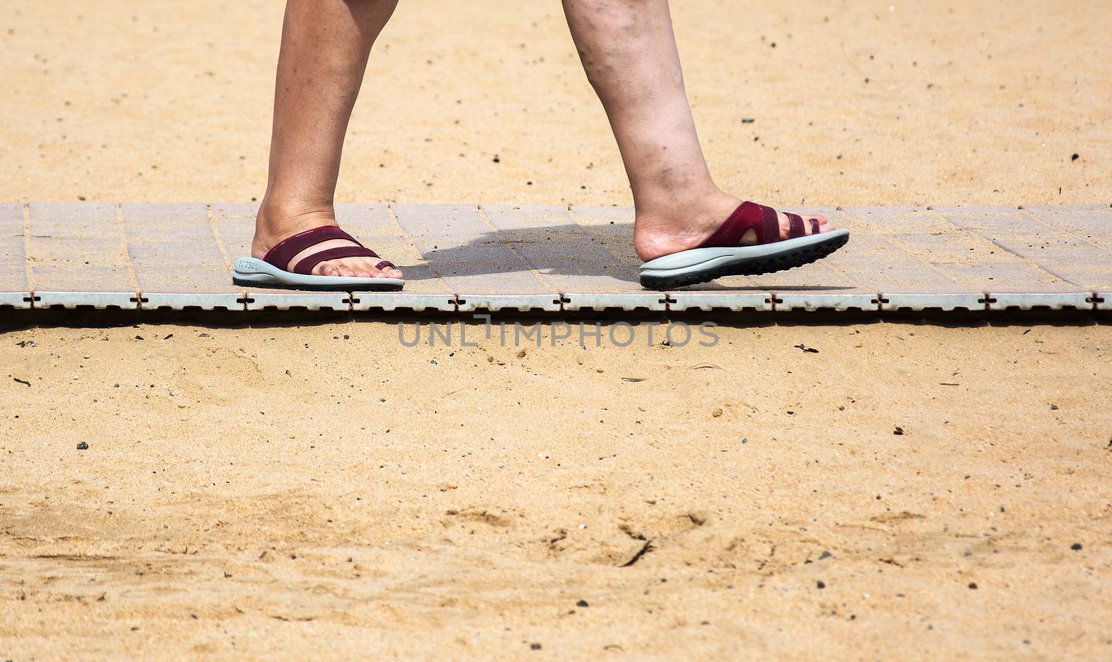 On the yellow sand beach lies on the path and there are feet in the summer slates

