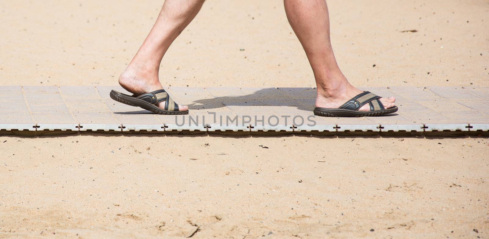 Men's feet in summer slates on the beach sand track by Grommik