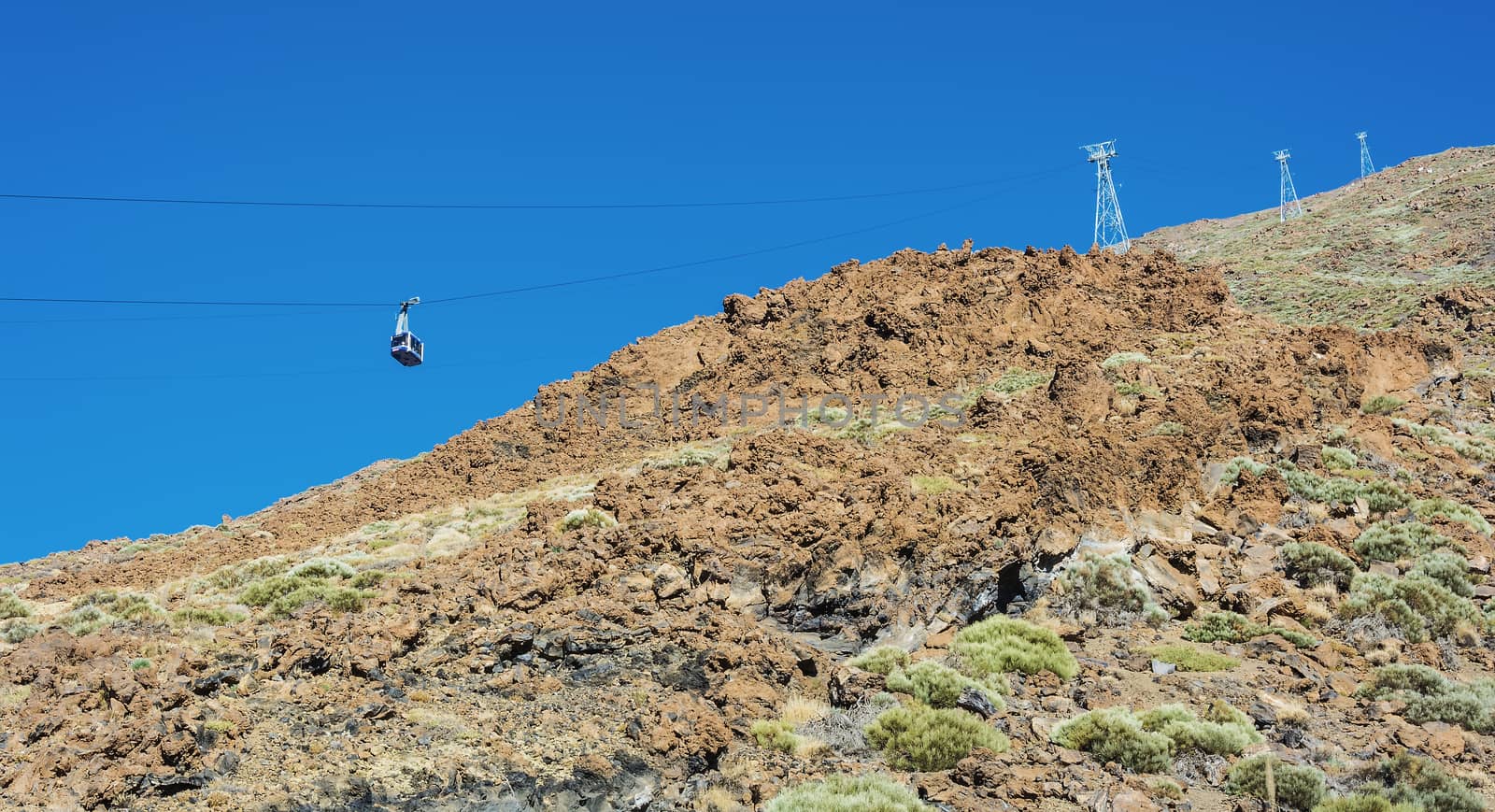 Blue cabin cable car with tourists climbing ropes stretched to the volcano Teide on Tenerife island.

