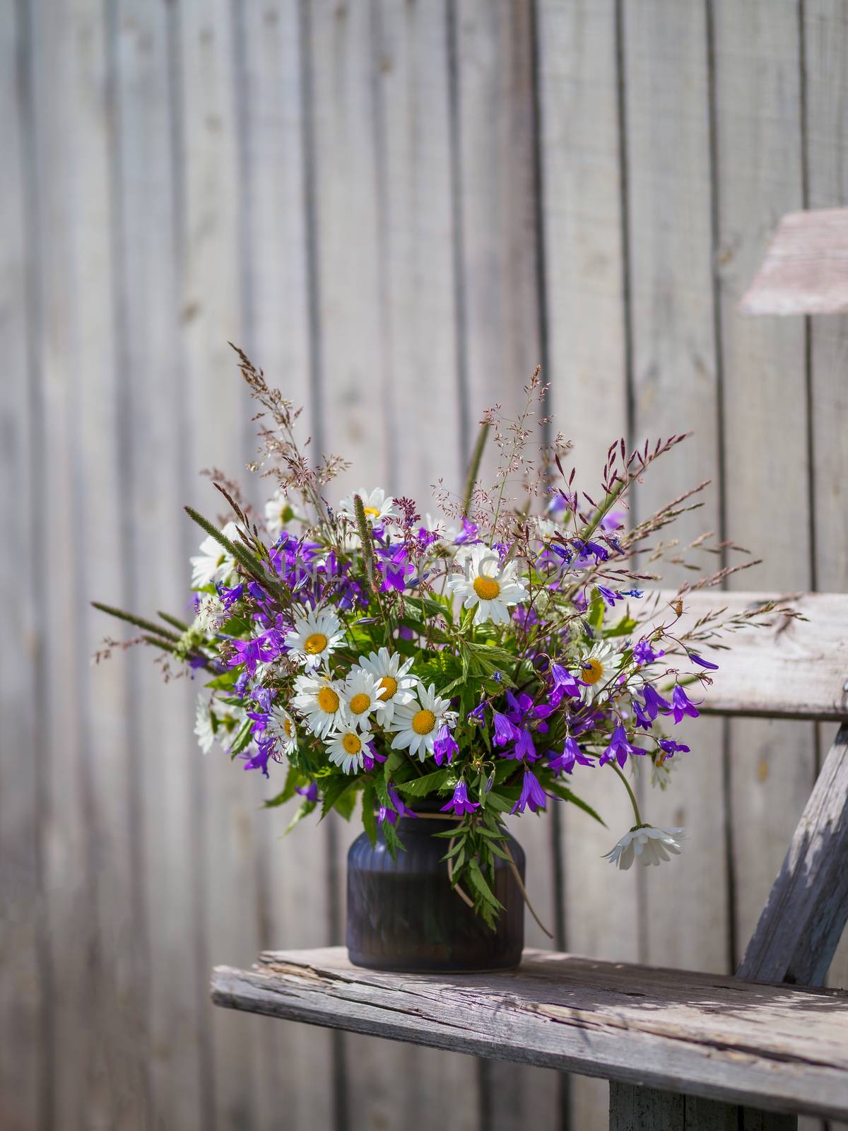 Bouqet with wild flowers on old wooden bench. Field flowers bouqet with campanula and camomile. Cottagecore and farmcore concept. Copy space